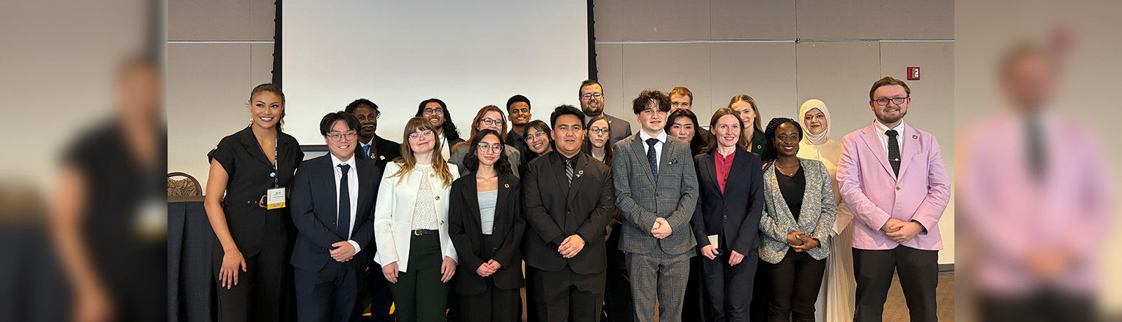 A large group of students stand together in front of a projector screen.