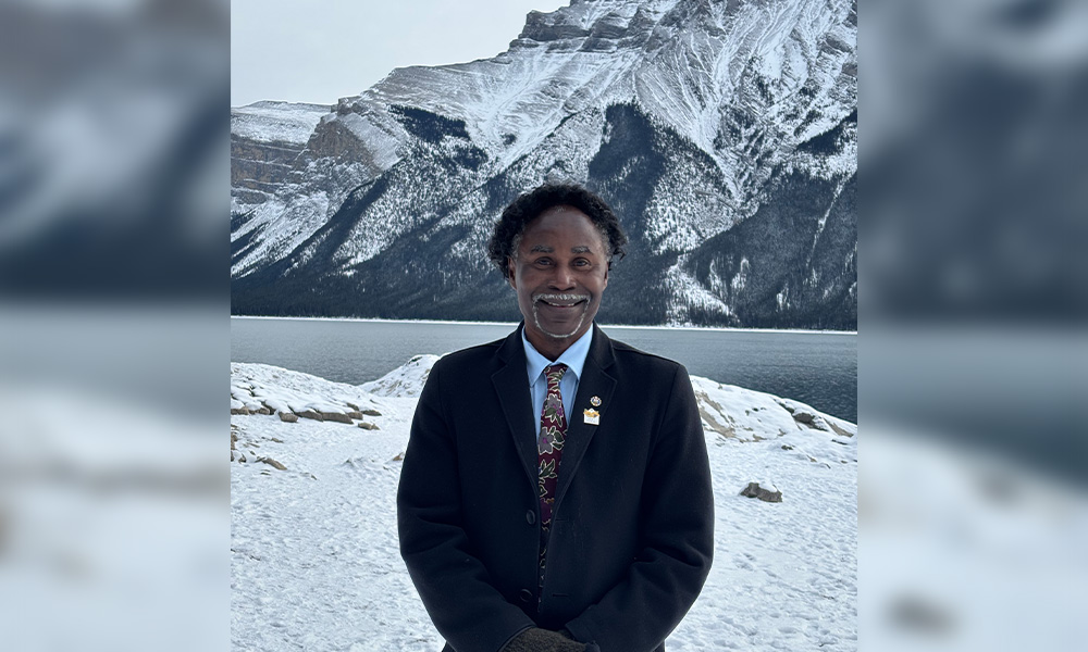 Dr. Chaldeans Mensah stands in front of a frozen lake and a snow-covered mountain.