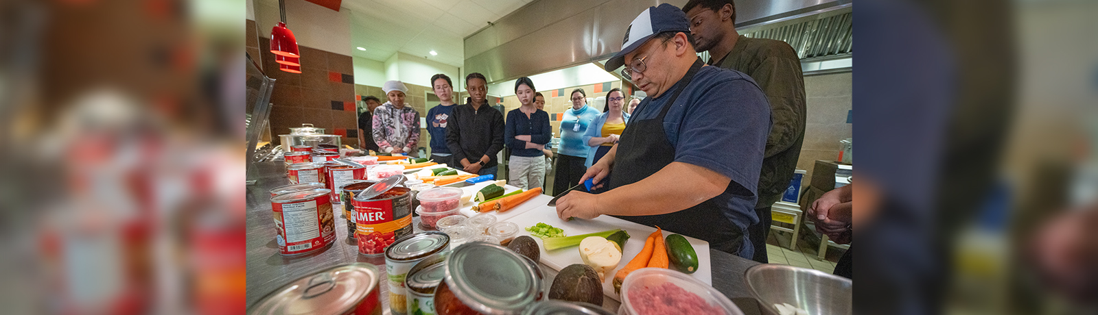 A group of people standing at a counter with food laid out and one person prepping food