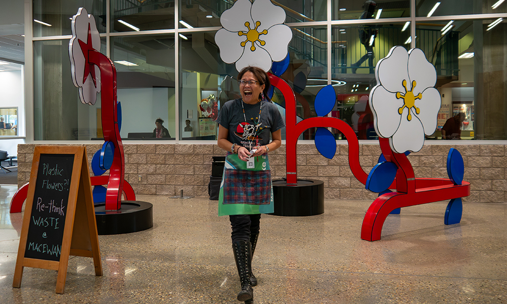 A woman stands laughing in front of a display of large plastic white flowers with red stems.