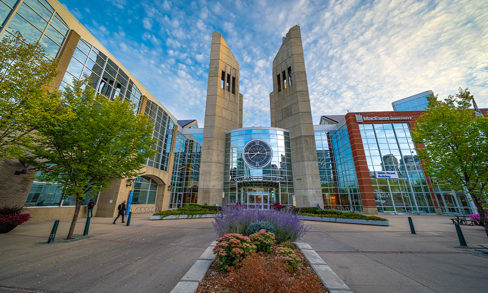A view of the clock tower entrance of MacEwan in an orange glow from a sunrise.