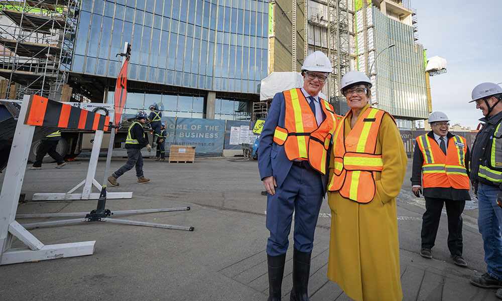 Hon. Myles McDougall and Dr. Annette Trimbee wear safety vests and hard hats while standing outside the new business building