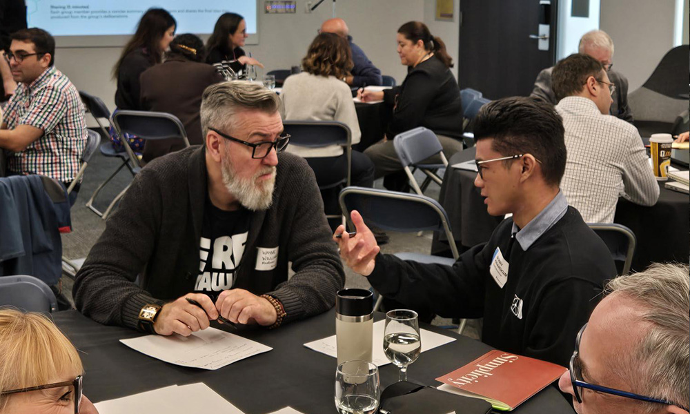 Attendees sit together at tables discussing and sharing ideas