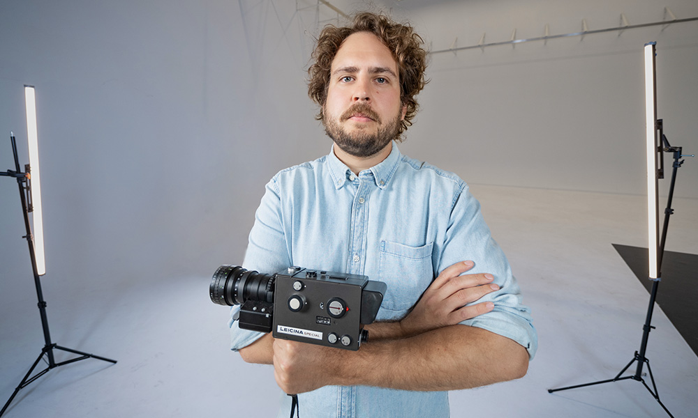 Waugh stands against a white background holding a Super 8 camera