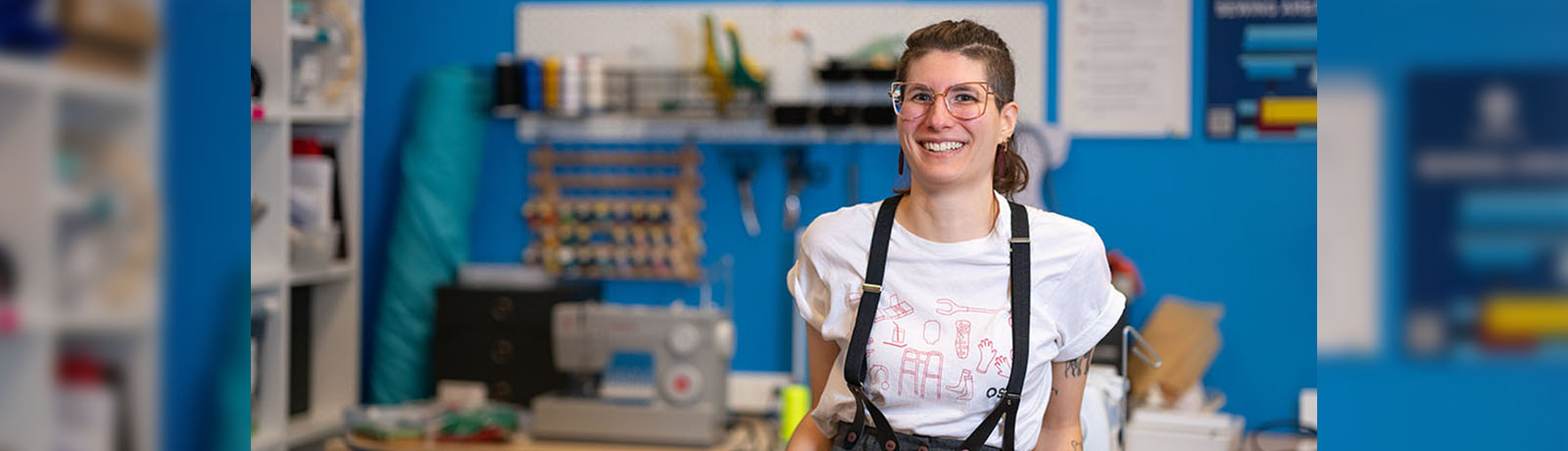 Jenna Dewar stands in the Makerspace with a sewing machine and supplies behind her
