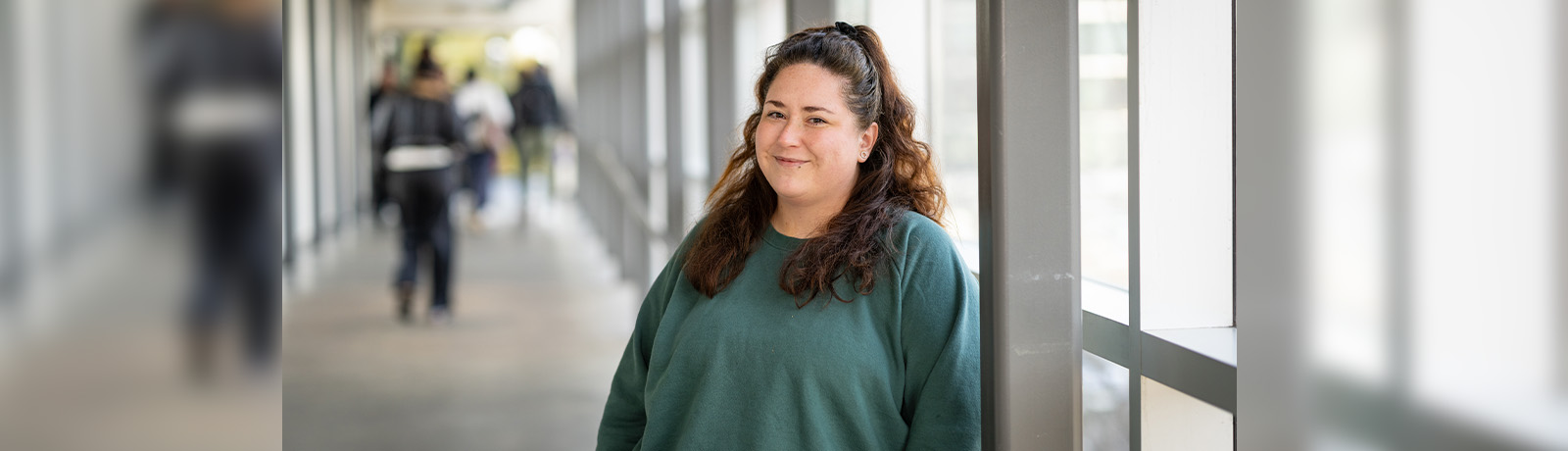 Diana Tymofichuk wears a green sweater and stands in the pedway between Building 9 and SAMU.