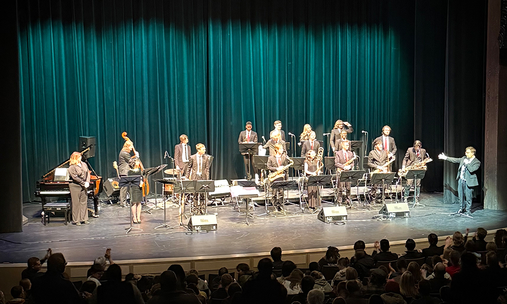 People holding instruments and dressed in black and white stand on stage with instruments. 