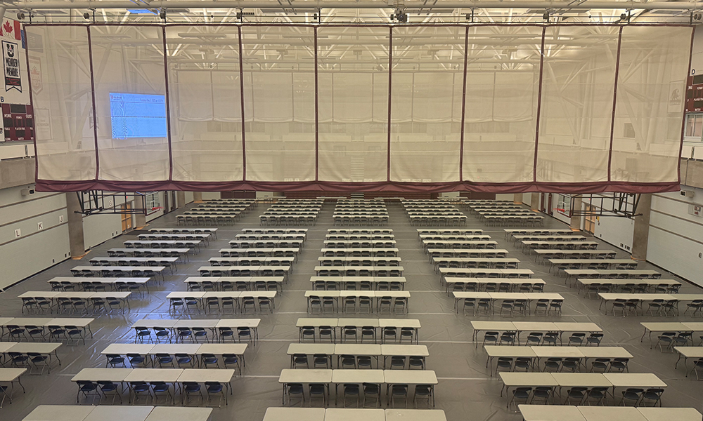 A large gymnasium set up with rows of desks and chairs.