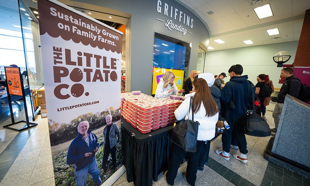 People stand around a table that has stacks of red containers holding pre-packaged potatoes.