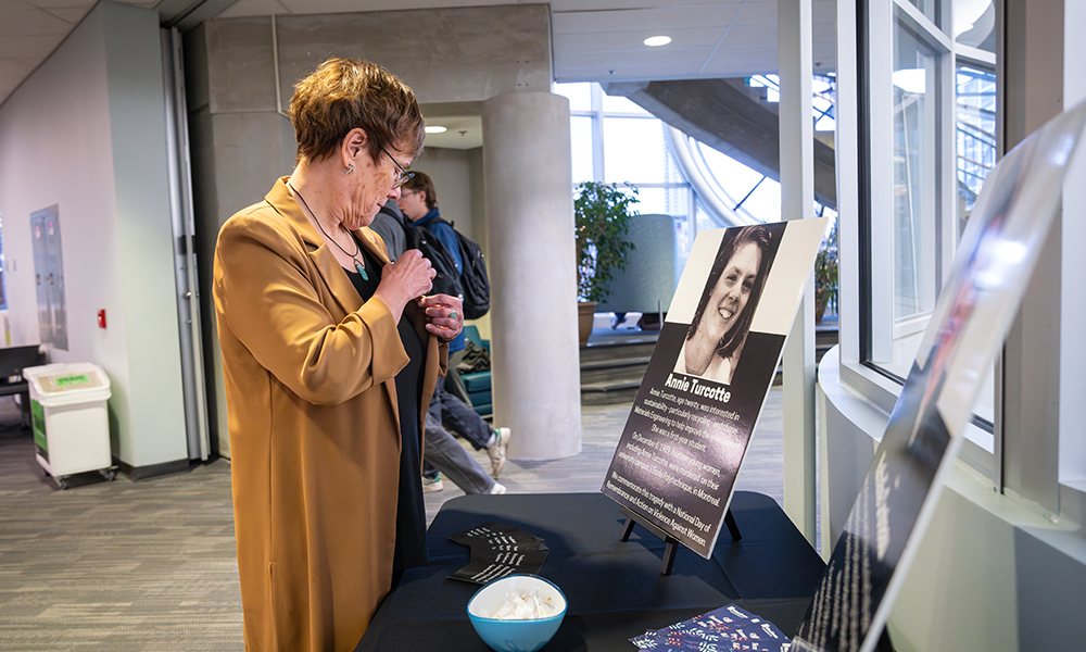 A woman placing a white ribbon on the lapel of her jacket, standing in front of a small table with a photography display.