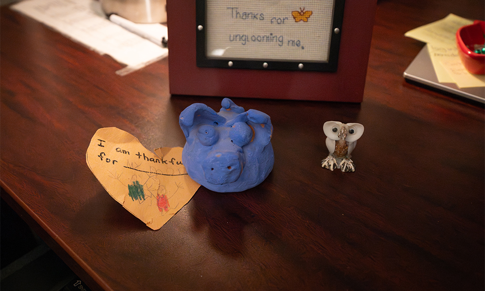 Small mementos including an orange paper heart that reads "I am thankful for my mom;" a handmade, clay blue pig; and a small owl made of shells.