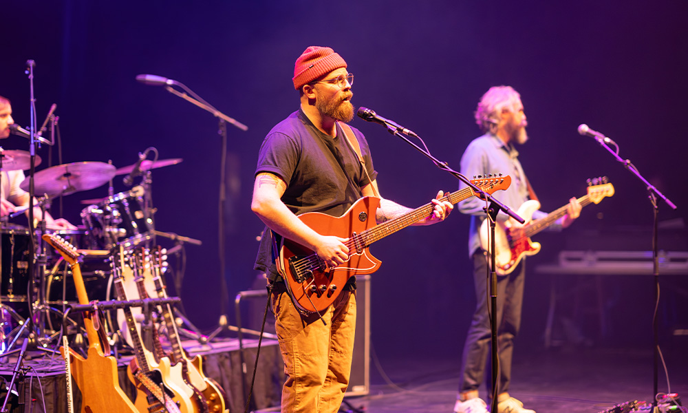 Two musicians stand on a stage, playing guitars and singing into microphones.