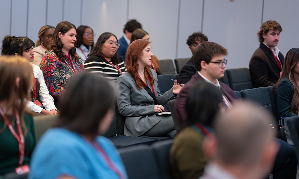 A student speaks amid an audience of other students, all facing toward the front of the room.