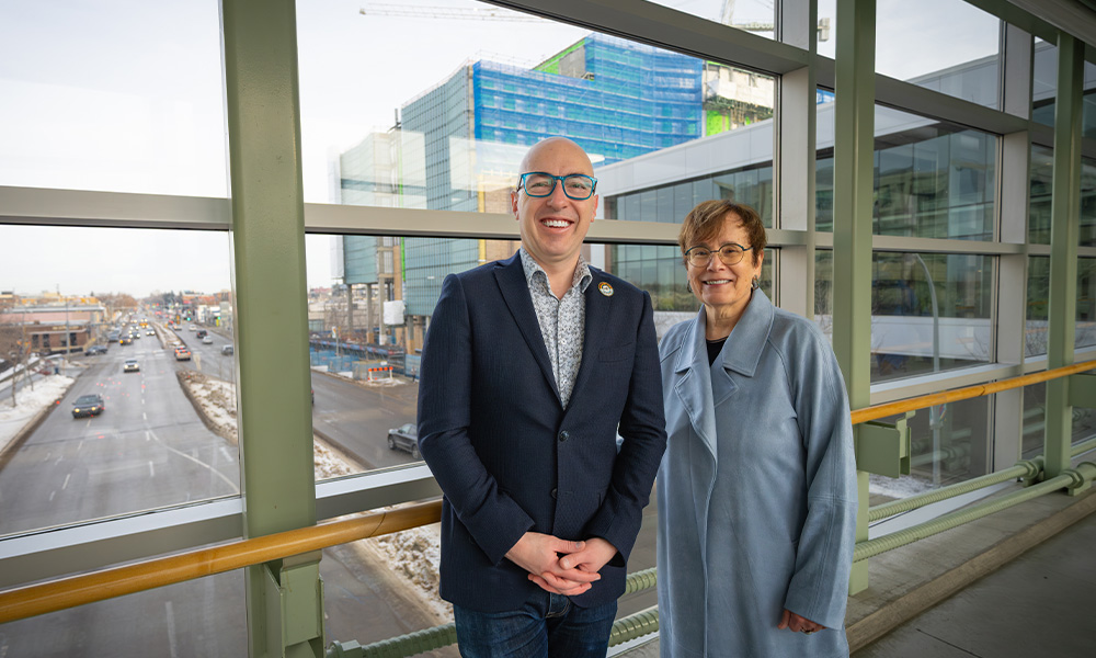 Mayor Andrew Knack and President and Vice-Chancellor Dr. Annette Trimbee stand together in the 109 St. pedway, with the School of Business Building construction visible behind them.