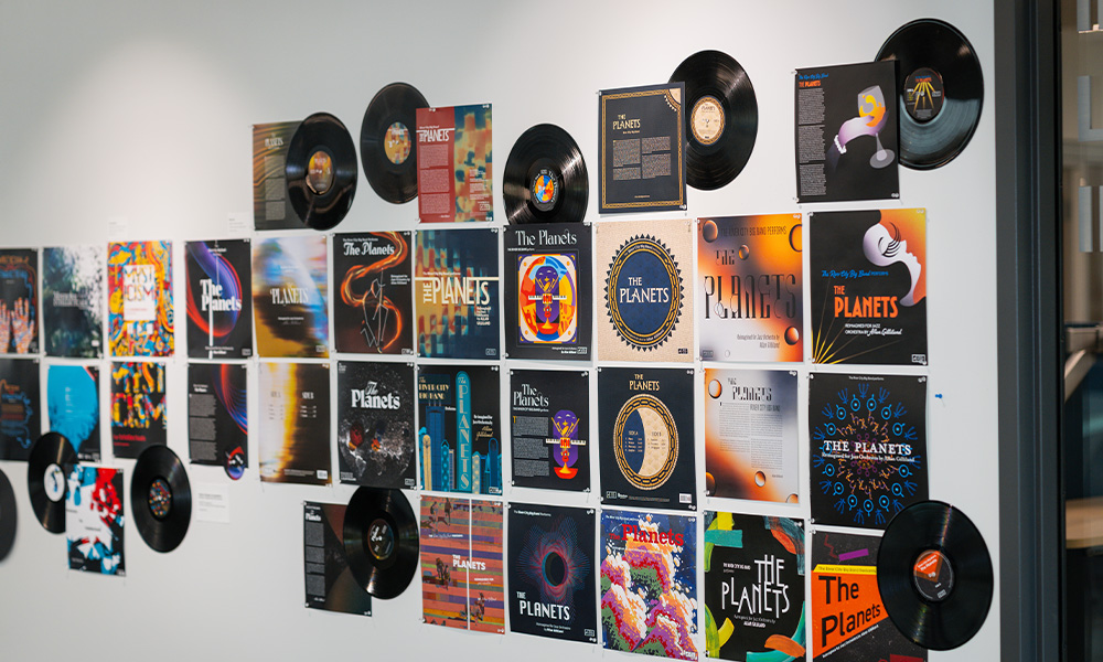 Album covers of all designs and colours hang on a white wall.