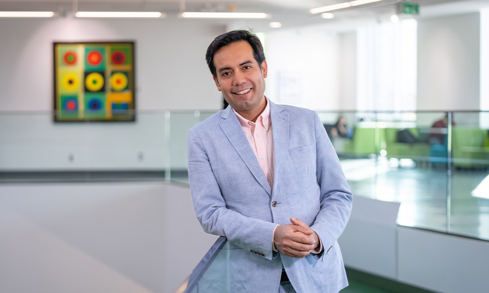 Fernando Ruiz-Angulo wears a grey suit jacket and leans against a railing in Allard Hall.