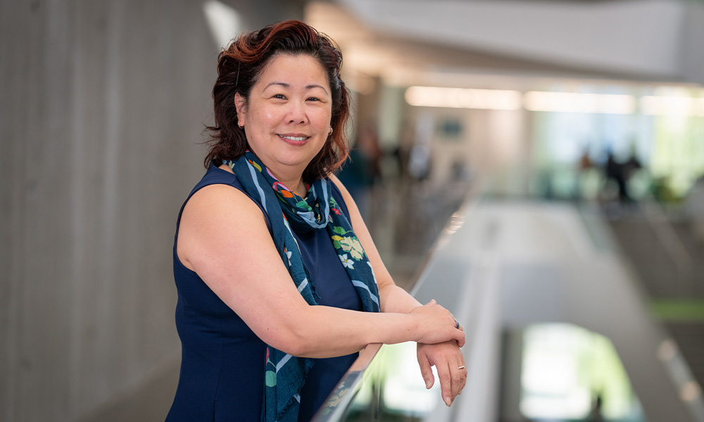 Sandy Jung leans her forearms against a glass railing in Allard Hall.