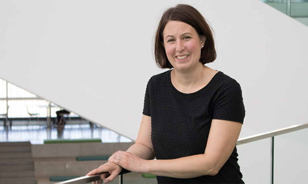 Emilie LeBel wears a black tee shirt and rests one arm on a railing.