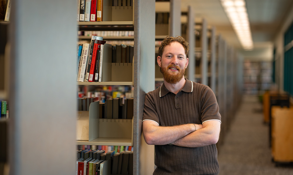 Kairo Martens leans against a bookcase in the library, arms folded over his chest.