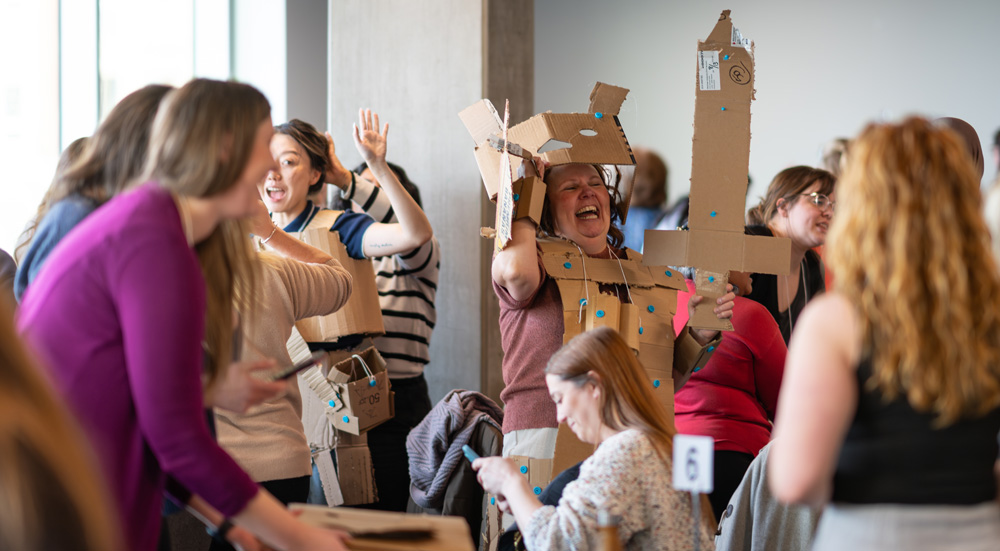 A room full of people make pieces of "clothing" out of cardboard boxes