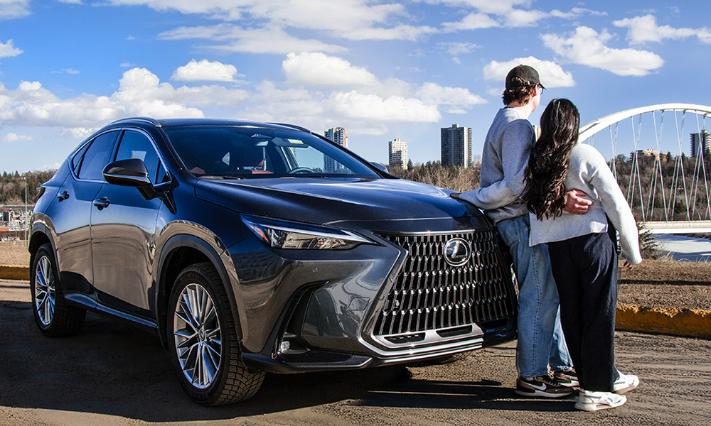 Two people lean against a new Lexus vehicle while looking eastward