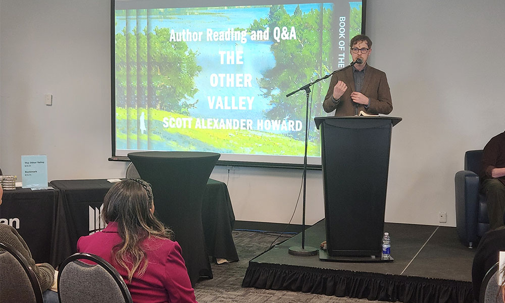 A man stands at the front of a room at a podium speaking into a microphone