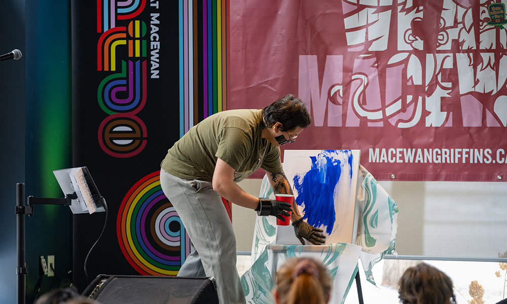 a person on a stage painting a blank canvas blue with their hands 