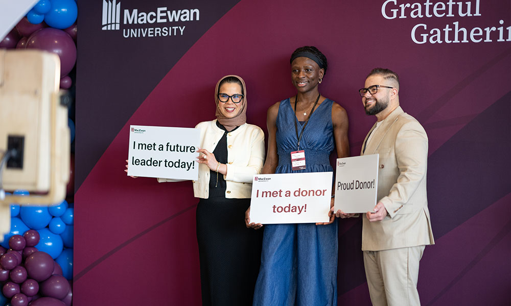 Three people stand at a photo booth station, each one holds a sign. Their signs read "I met a future leader today", "I met a donor today" and "Proud Donor" 