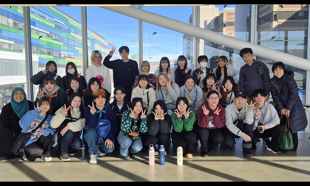 A group of students pose in front of a wall of windows
