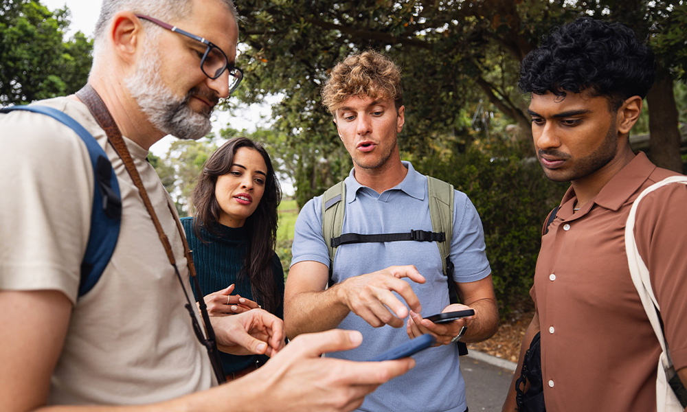 Four people stand together, two holding cell phones, all appearing to discuss what they're seeing on the screens.