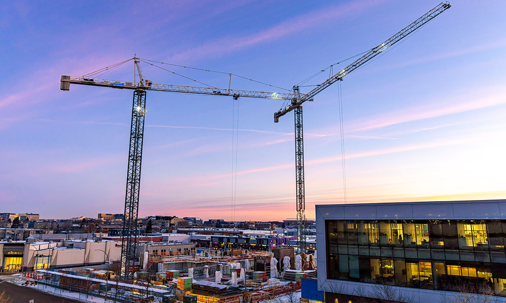 A sunset photo, the sky is grey, two cranes are erected into the air. 