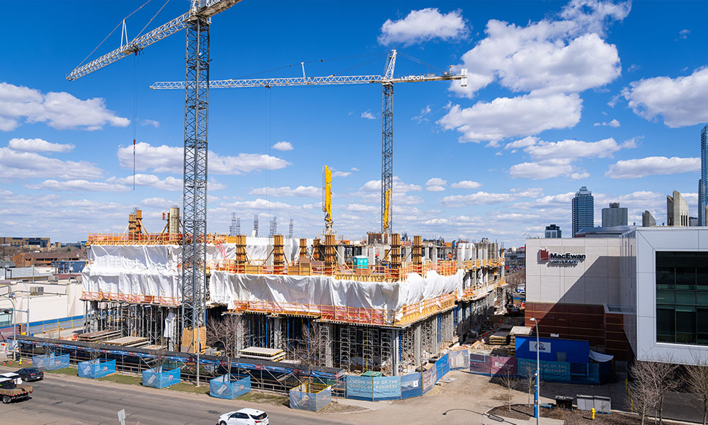A large construction site that contains two floors of a building covered in plastic, two cranes are erected at the site. 