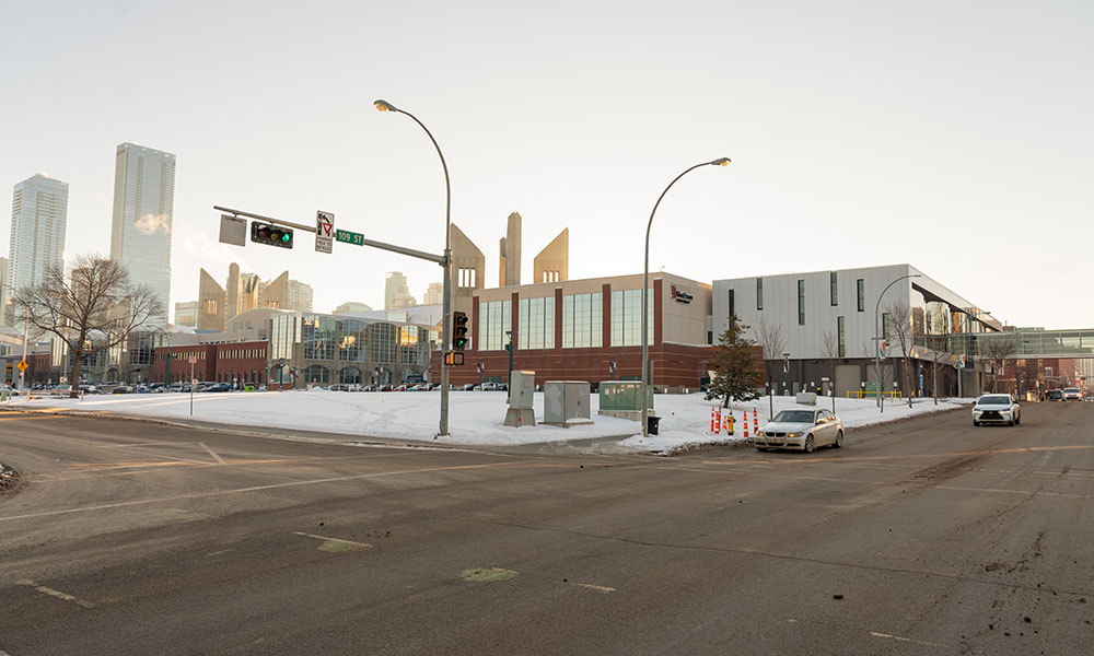 A winter scene of an intersection in a city, with a white and brick building. 