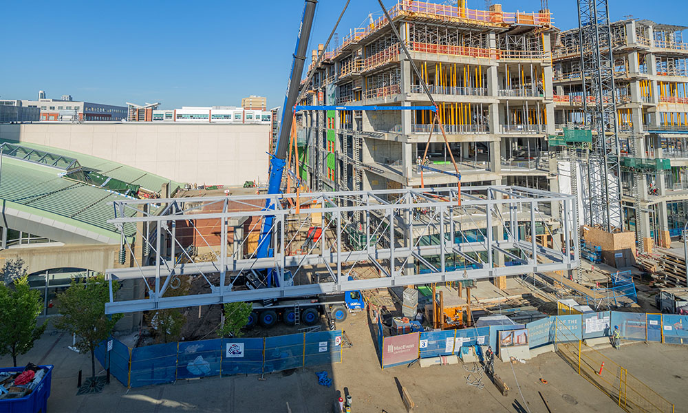 The concrete frame of the full building in the background, as well as a crane, and in the foreground a horizontal, white metal pedway