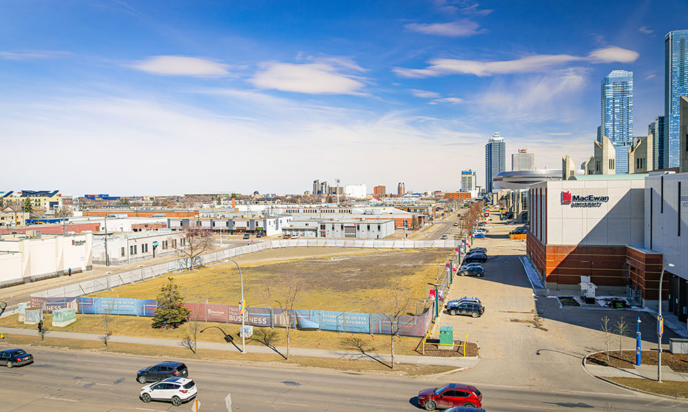 An empty field surrounded by construction fencing, a downtown cityscape in the distance