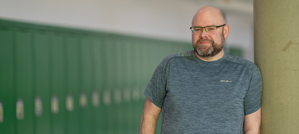 Dr. Michael J. Vekasi leans against a column in front of a row of green lockers
