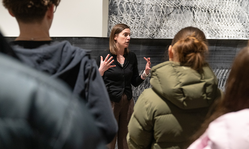 A woman stands in front of a crowd, speaking.