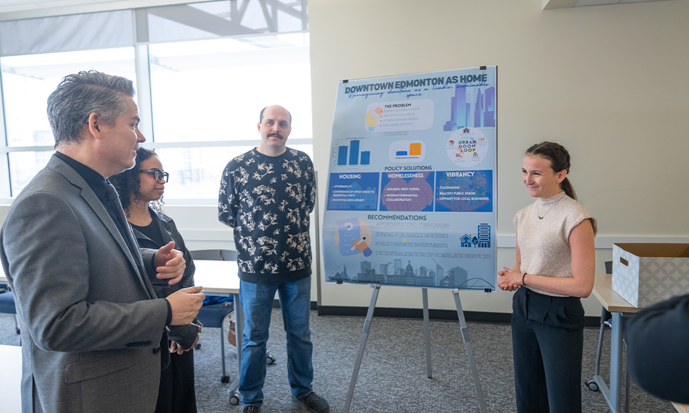 Three people listen to a student explain her research.