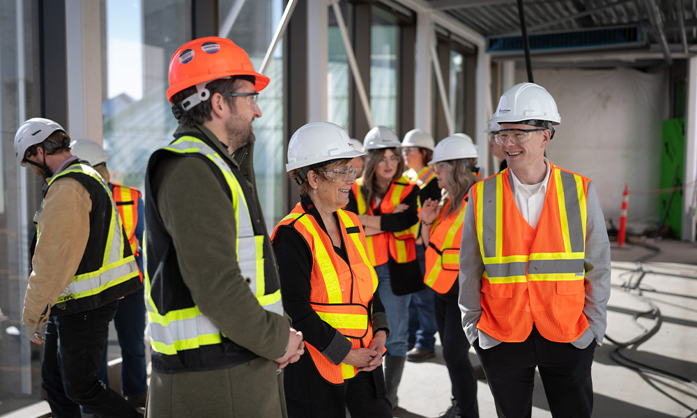 Three people in high-vis vests and hard hats smile in a construction site.
