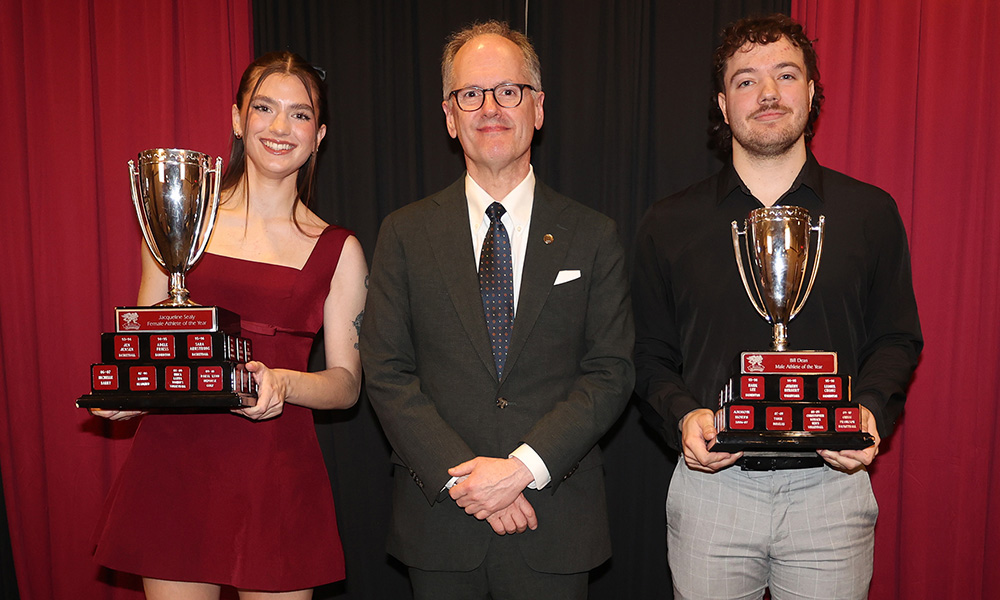 Two students hold trophies on either side of Dr. Monk.