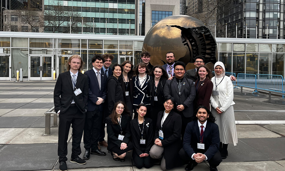 A group of students poses in front of a silver sphere in NYC.