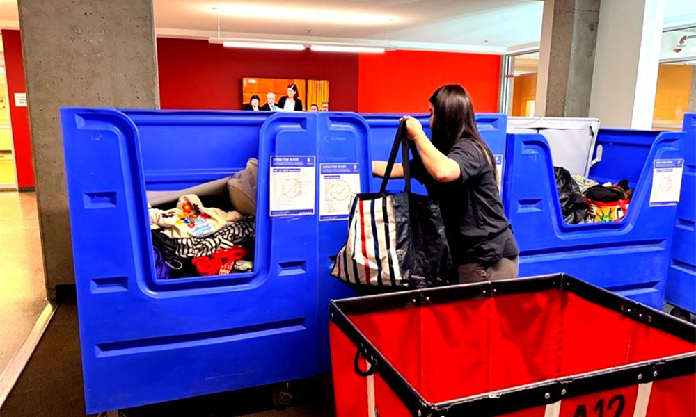 A woman lifts items into a massive blue bin.