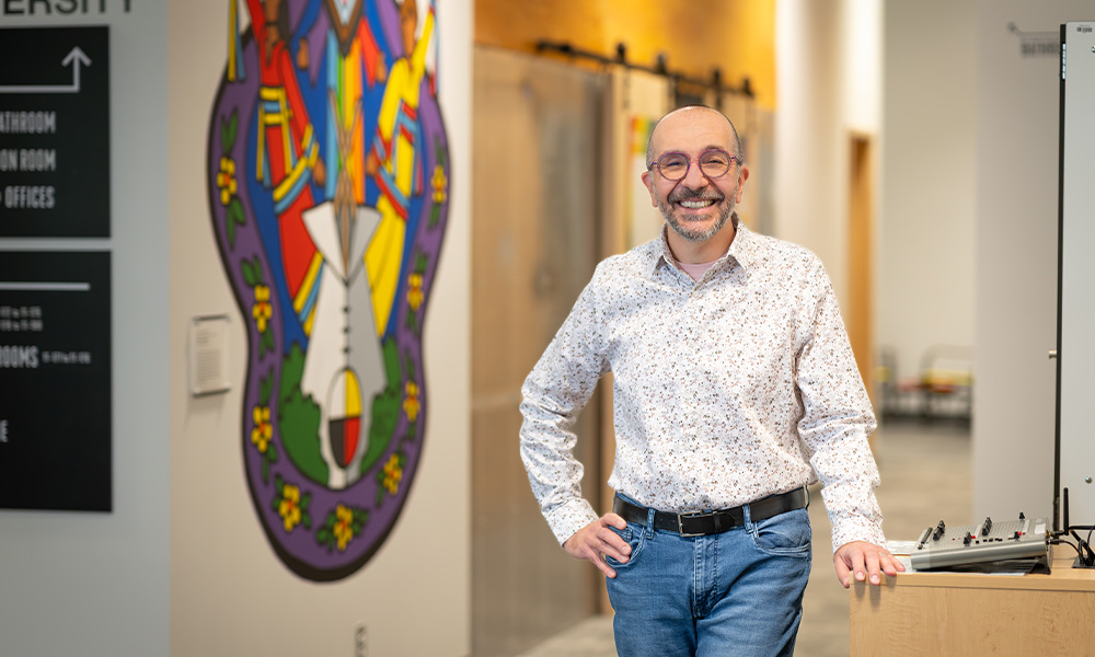 Dr. Alessio Ponzio smiles in front of the mural in CSGD.