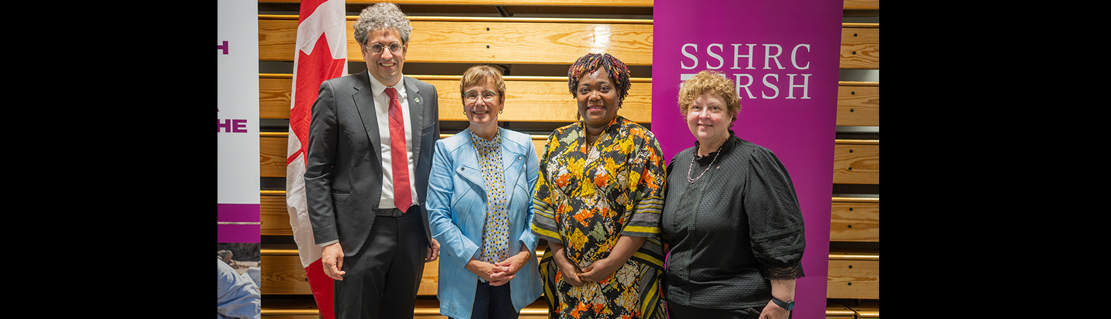 Four people stand against a wooden backdrop in front of a SSHRC banner on a purple background