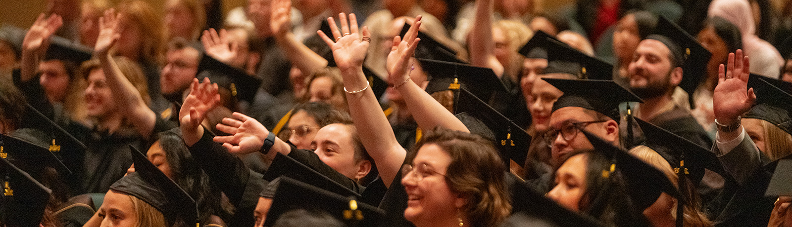 People in caps and gowns smile and wave toward the stage in the Winspear Centre.