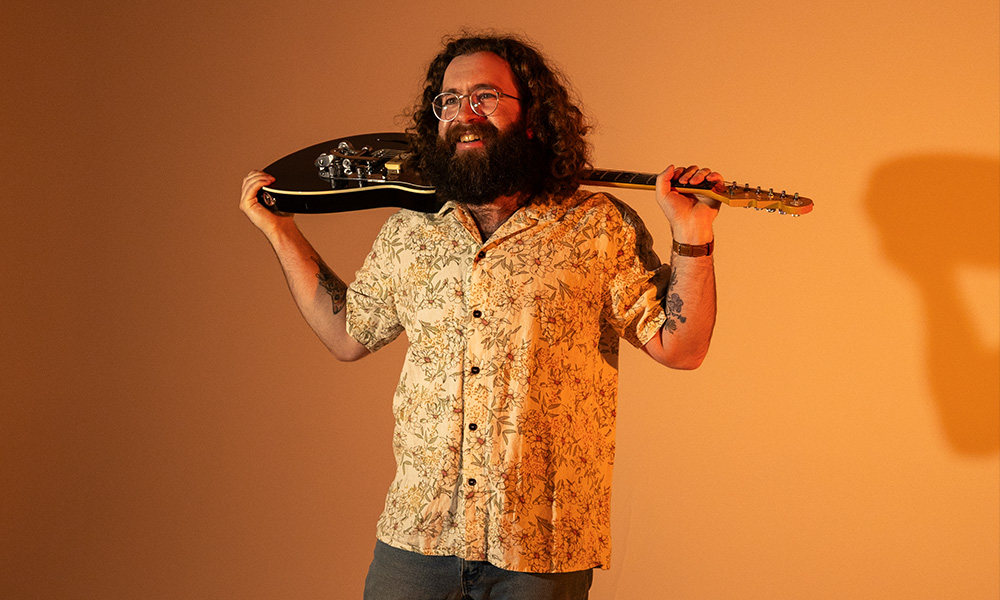 A man holds a guitar on his sounders on a golden background