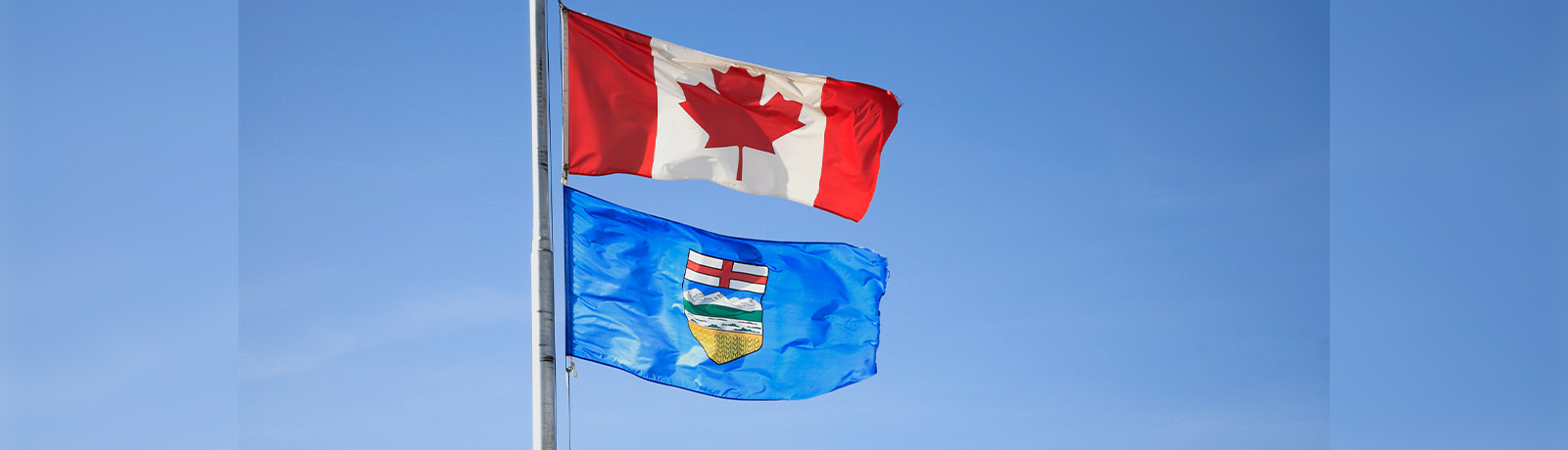 A Canadian flag and an Alberta flag being flown on the same flagpole.