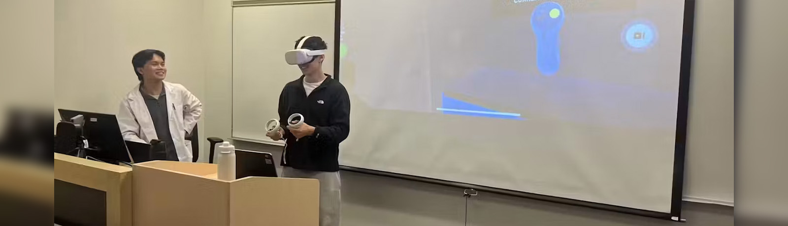 One student wears VR goggles while another watches and smiles.