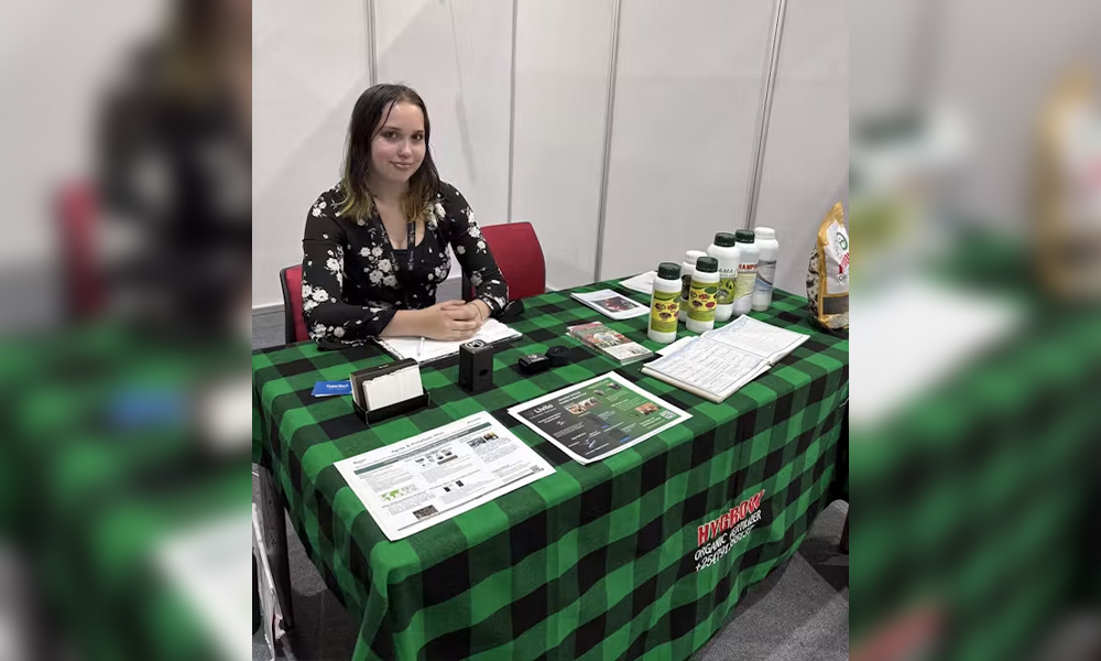 A woman sits at a booth with a green checkered tablecloth and products lined up on it.