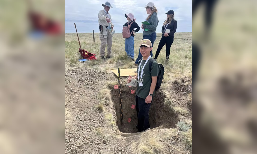 A man stands in a hold dug into the earth, measuring the depth.